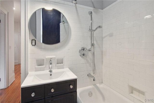 bathroom featuring hardwood / wood-style floors, vanity, tiled shower / bath combo, and backsplash