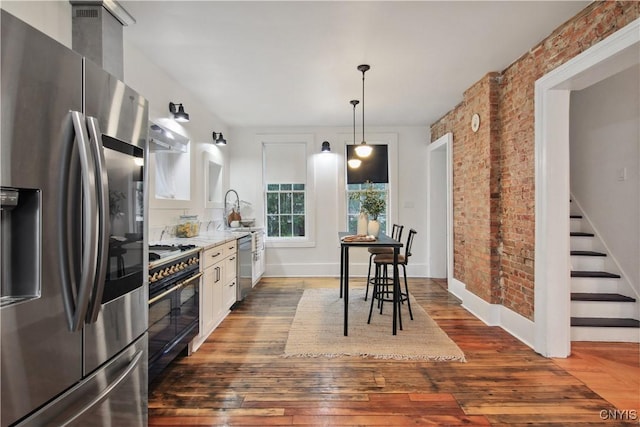 kitchen with brick wall, stainless steel appliances, dark hardwood / wood-style floors, white cabinetry, and hanging light fixtures