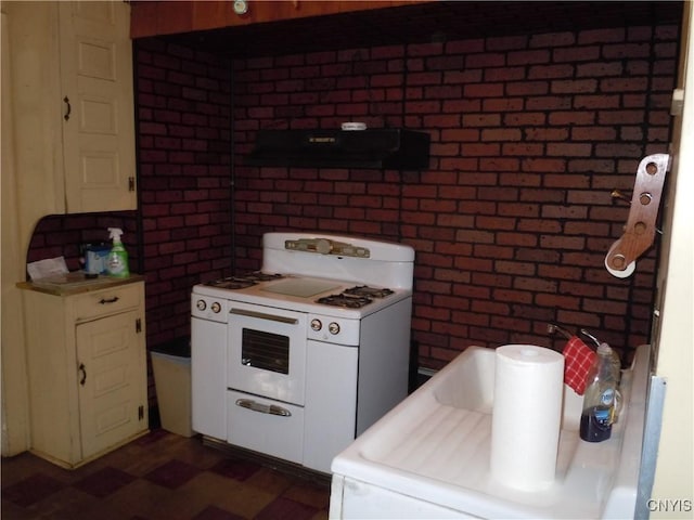 kitchen featuring exhaust hood, white cabinets, white range oven, washer / dryer, and brick wall