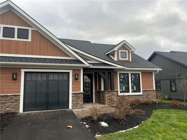 craftsman house with an attached garage, stone siding, a shingled roof, and aphalt driveway