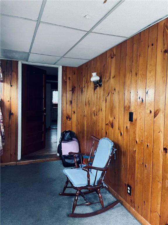 sitting room featuring a paneled ceiling, dark carpet, and wood walls