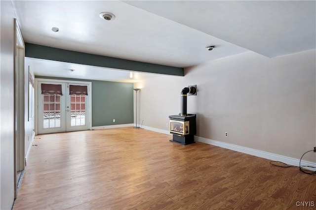 unfurnished living room with beamed ceiling, light hardwood / wood-style floors, a wood stove, and french doors