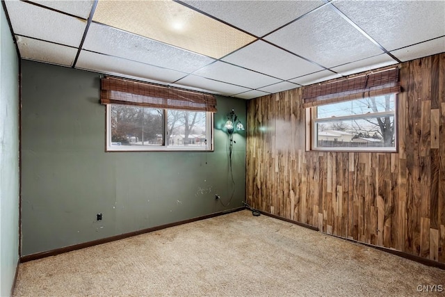 basement featuring wooden walls, a drop ceiling, and light carpet