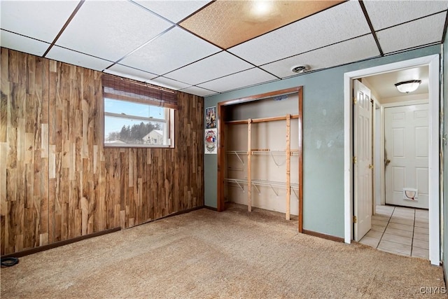 unfurnished bedroom with a paneled ceiling, wooden walls, a closet, and light carpet