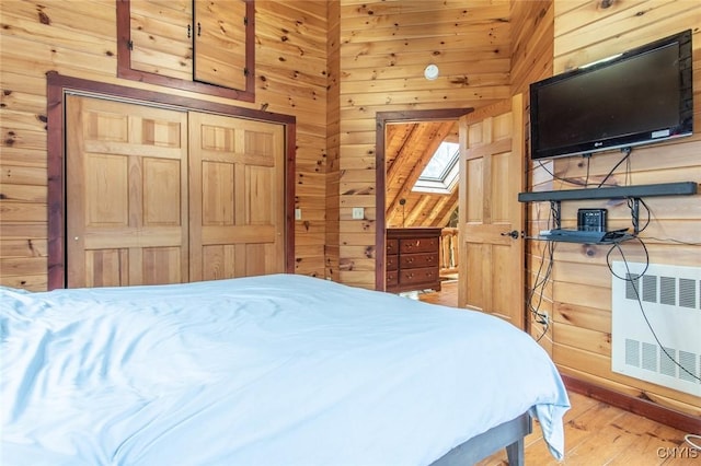 bedroom featuring hardwood / wood-style floors, wood walls, a closet, a skylight, and heating unit