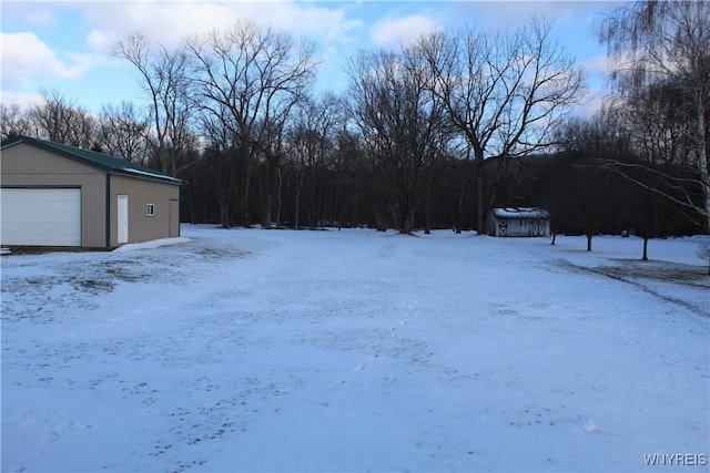 yard layered in snow featuring a garage and an outbuilding