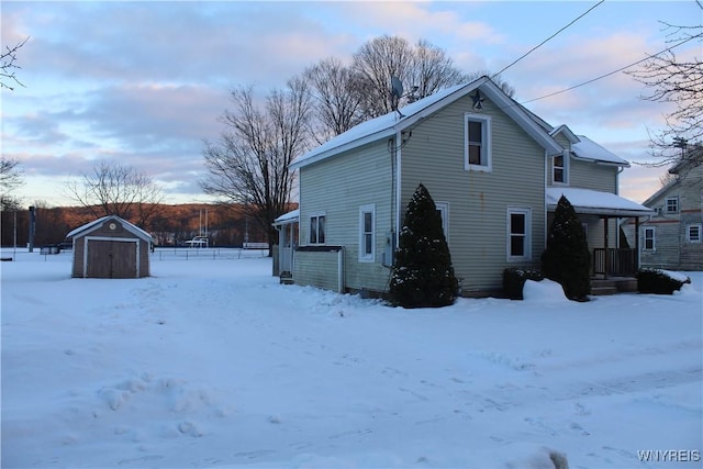 snow covered rear of property featuring a shed