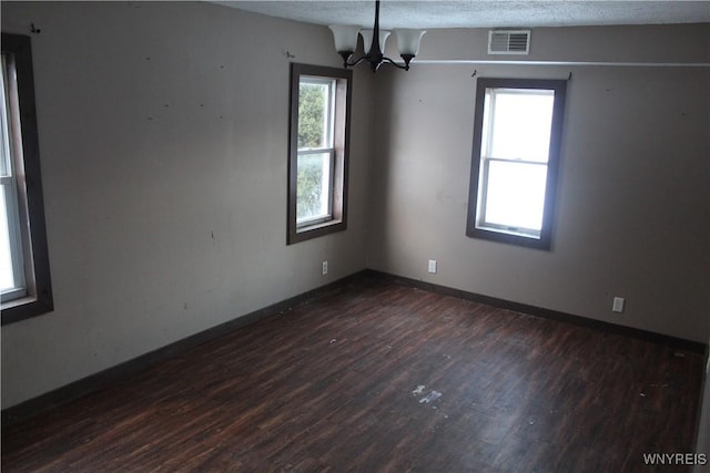 empty room featuring a textured ceiling, an inviting chandelier, and dark wood-type flooring