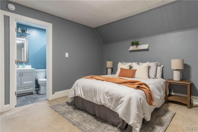 bedroom with ensuite bathroom, vaulted ceiling, and light colored carpet