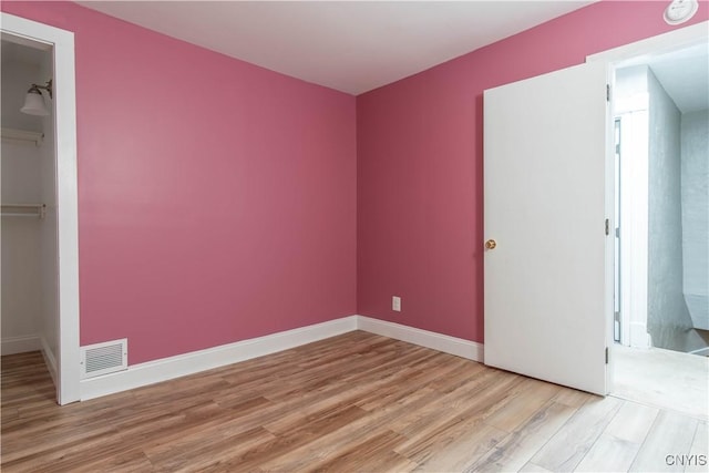 unfurnished bedroom featuring a spacious closet, light hardwood / wood-style flooring, and a closet