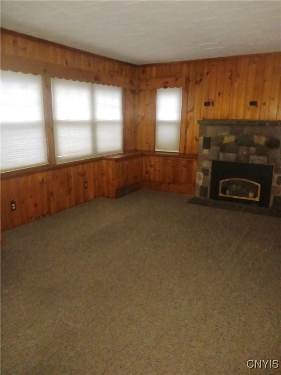 unfurnished living room featuring carpet flooring, a stone fireplace, and wooden walls