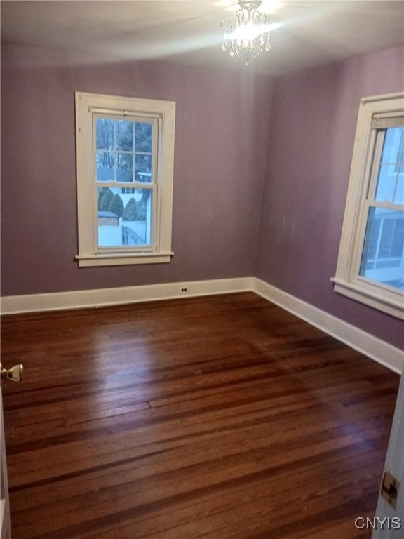 empty room with dark wood-type flooring and an inviting chandelier