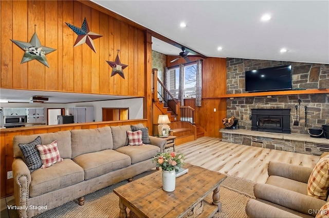 living room with ceiling fan, wood-type flooring, a fireplace, lofted ceiling, and wood walls