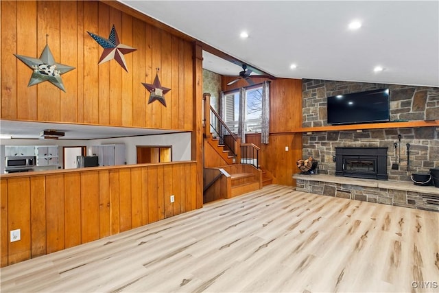 unfurnished living room with a fireplace, wood walls, light hardwood / wood-style flooring, and vaulted ceiling