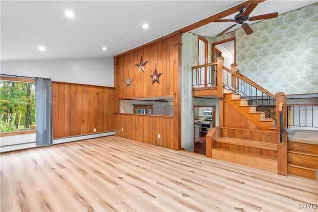 unfurnished living room with lofted ceiling, wooden walls, ceiling fan, baseboard heating, and light hardwood / wood-style floors