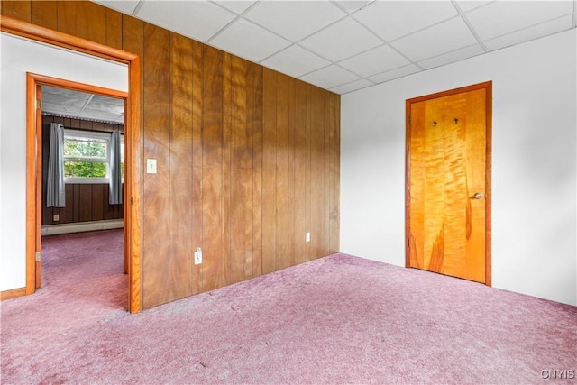 carpeted spare room featuring a drop ceiling, baseboard heating, and wooden walls