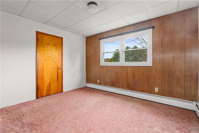 carpeted spare room featuring baseboard heating, wood walls, and a drop ceiling