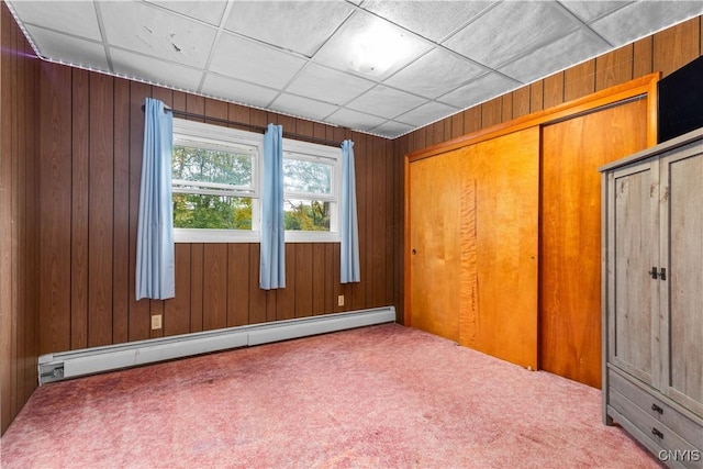 unfurnished bedroom with carpet flooring, a baseboard radiator, a closet, and wood walls