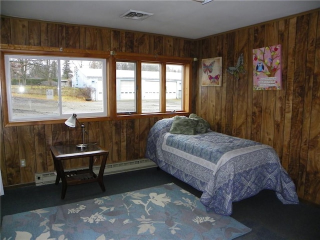 bedroom with wooden walls, dark carpet, and a baseboard heating unit