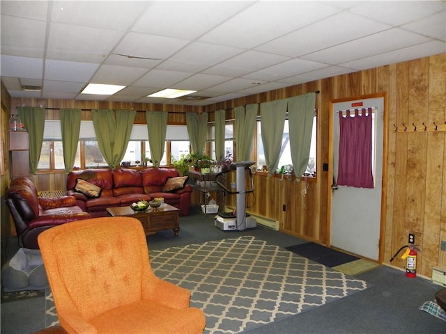 carpeted living room featuring a paneled ceiling, wood walls, and a baseboard radiator