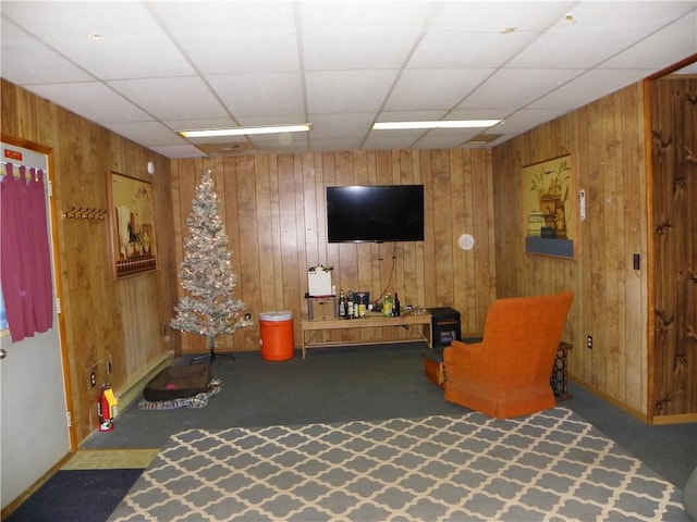 living area with carpet flooring, a drop ceiling, and wooden walls