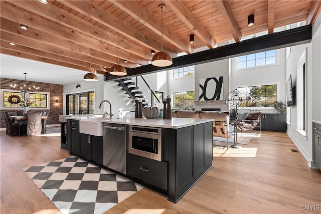 kitchen with a wealth of natural light, stainless steel appliances, hanging light fixtures, brick wall, and a center island with sink