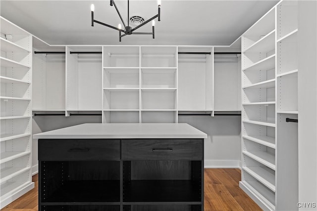 walk in closet with dark wood-type flooring and a chandelier