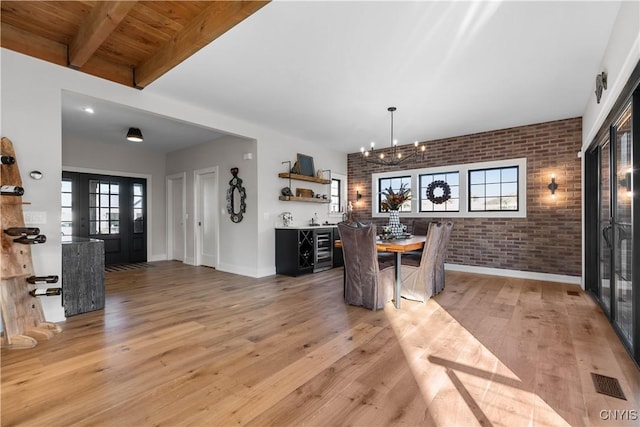 dining area with wooden ceiling, an inviting chandelier, beamed ceiling, light hardwood / wood-style floors, and brick wall