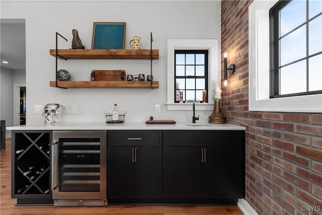 bar with sink, beverage cooler, brick wall, and light wood-type flooring