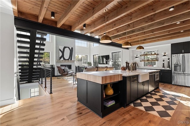 kitchen with a high ceiling, a center island with sink, appliances with stainless steel finishes, beamed ceiling, and decorative light fixtures