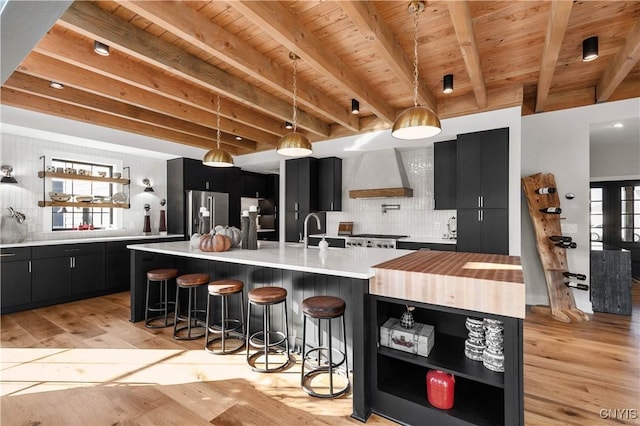 kitchen featuring stainless steel appliances, hanging light fixtures, tasteful backsplash, a large island with sink, and custom exhaust hood