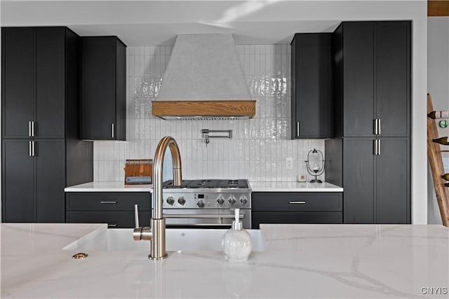 kitchen featuring tasteful backsplash, light stone countertops, high end range, and custom range hood