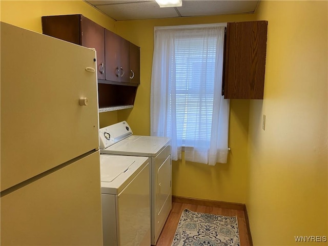 clothes washing area featuring cabinets, light wood-type flooring, a healthy amount of sunlight, and washing machine and clothes dryer