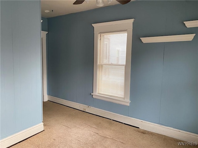 carpeted empty room with ceiling fan and wood walls