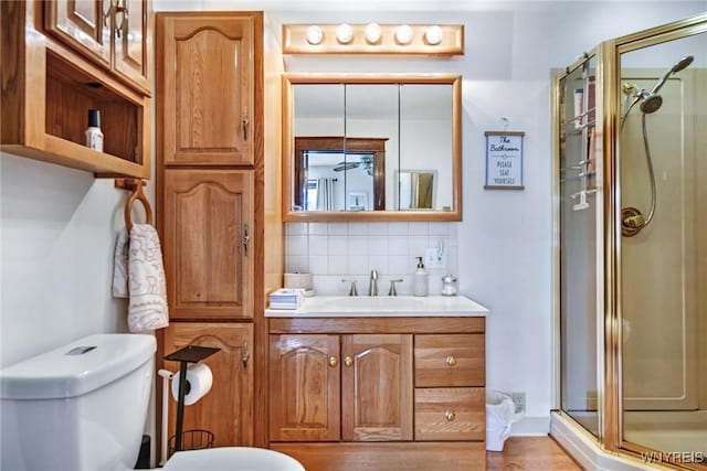 bathroom with vanity, toilet, a shower with shower door, and backsplash