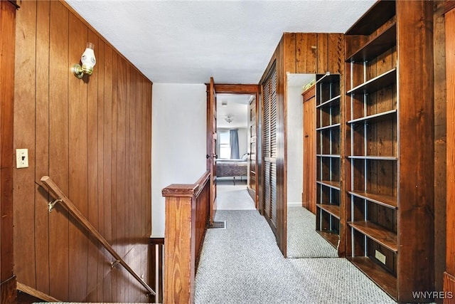 hallway with light colored carpet, a textured ceiling, and wood walls