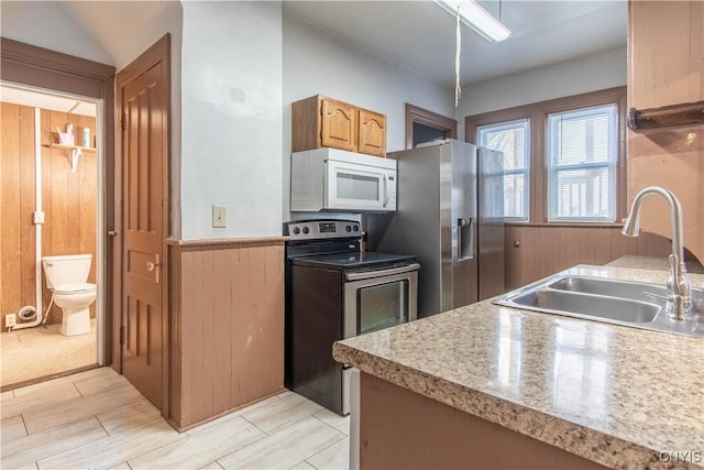 kitchen featuring stainless steel appliances, vaulted ceiling, wooden walls, and sink