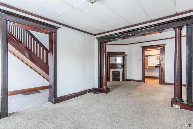 unfurnished living room with light colored carpet, a drop ceiling, and ornamental molding