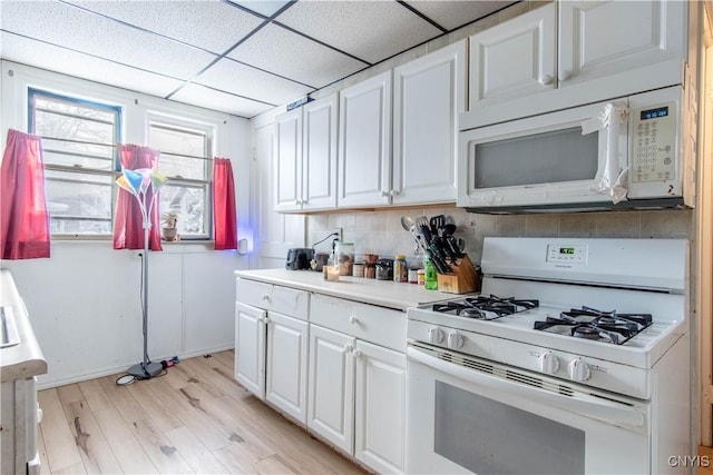 kitchen with white cabinetry, a drop ceiling, white appliances, decorative backsplash, and light wood-type flooring