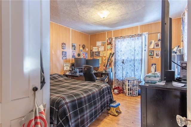 bedroom featuring a textured ceiling, light hardwood / wood-style flooring, and wood walls