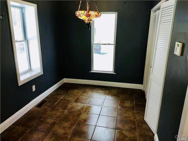 unfurnished dining area featuring a chandelier, dark tile patterned flooring, and plenty of natural light