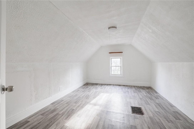 bonus room featuring a textured ceiling, light wood-type flooring, and lofted ceiling