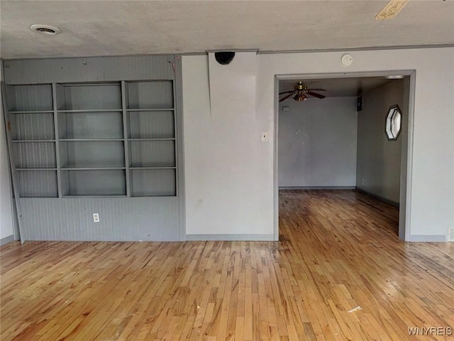 empty room with ceiling fan, light wood-type flooring, and a textured ceiling