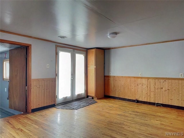 empty room with plenty of natural light, light hardwood / wood-style floors, french doors, and ornamental molding