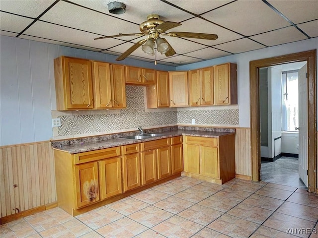 kitchen with decorative backsplash, ceiling fan, wooden walls, and sink