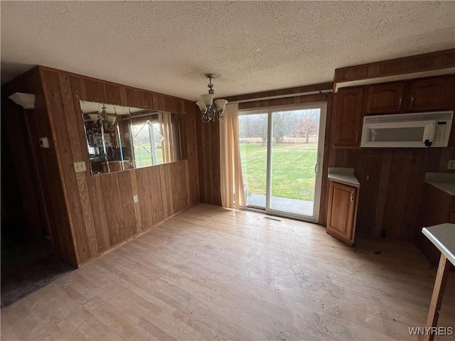 unfurnished dining area with plenty of natural light, light hardwood / wood-style flooring, a textured ceiling, and an inviting chandelier