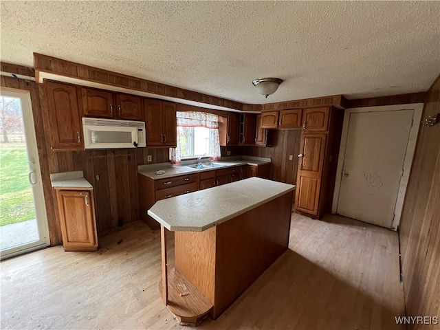 kitchen with sink, a textured ceiling, wooden walls, a kitchen island, and light wood-type flooring