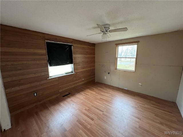 empty room featuring a textured ceiling, light hardwood / wood-style floors, ceiling fan, and wooden walls