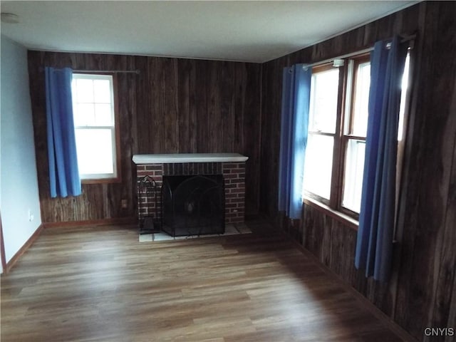 unfurnished living room featuring wood-type flooring, a brick fireplace, a wealth of natural light, and wood walls