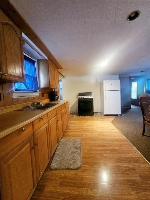 kitchen featuring black gas stove, white refrigerator, light hardwood / wood-style floors, and a textured ceiling